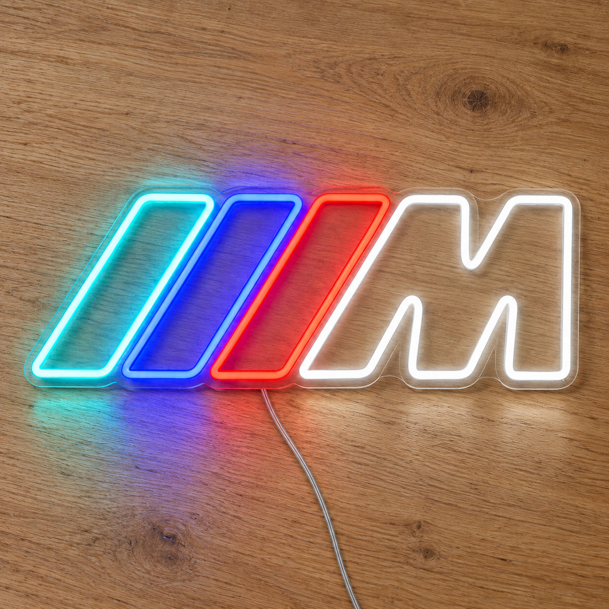 BMW M LED Neon Sign in blue, red and white, featuring BMW M logo with three coloured stripes on a wooden surface.