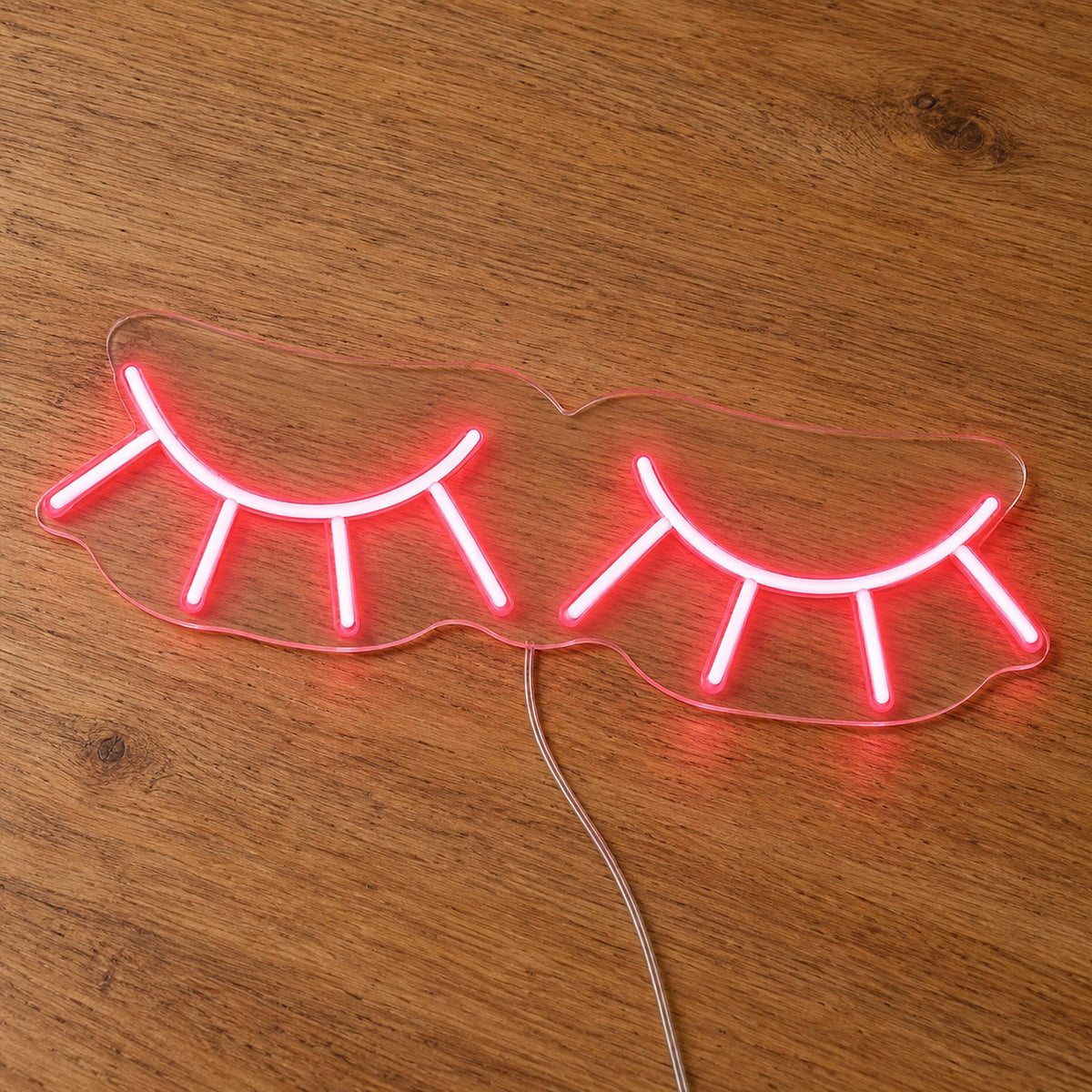 Eyelashes LED Neon Light Sign in pink, featuring two closed eyelash outlines on a wooden surface.