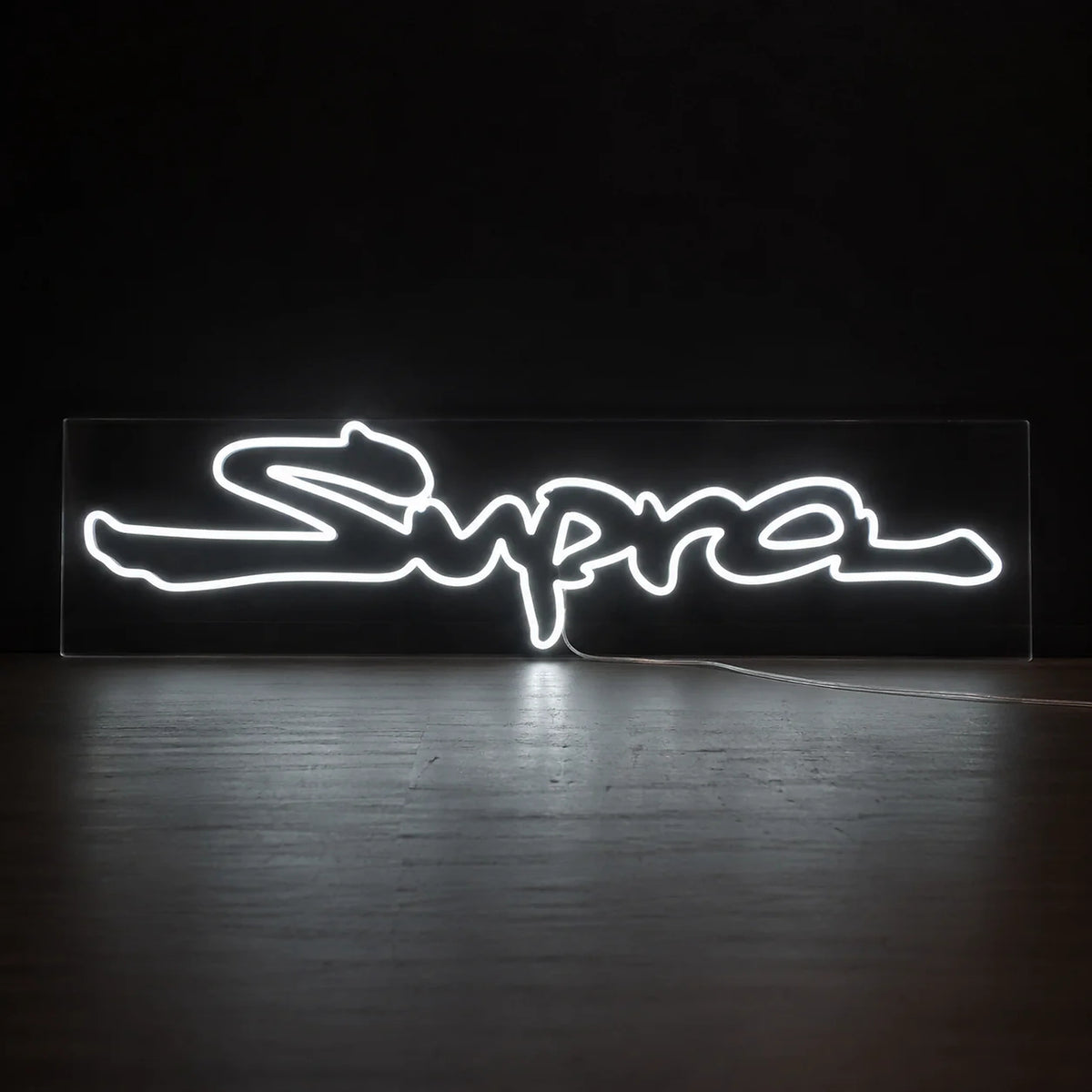 Toyota Supra Logo Neon Sign in white, featuring Supra script logo against a dark wall.