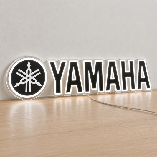 Yamaha (Black) LED Neon Sign in white, featuring Yamaha lettering beside a tuning-fork emblem on a light reflective surface.