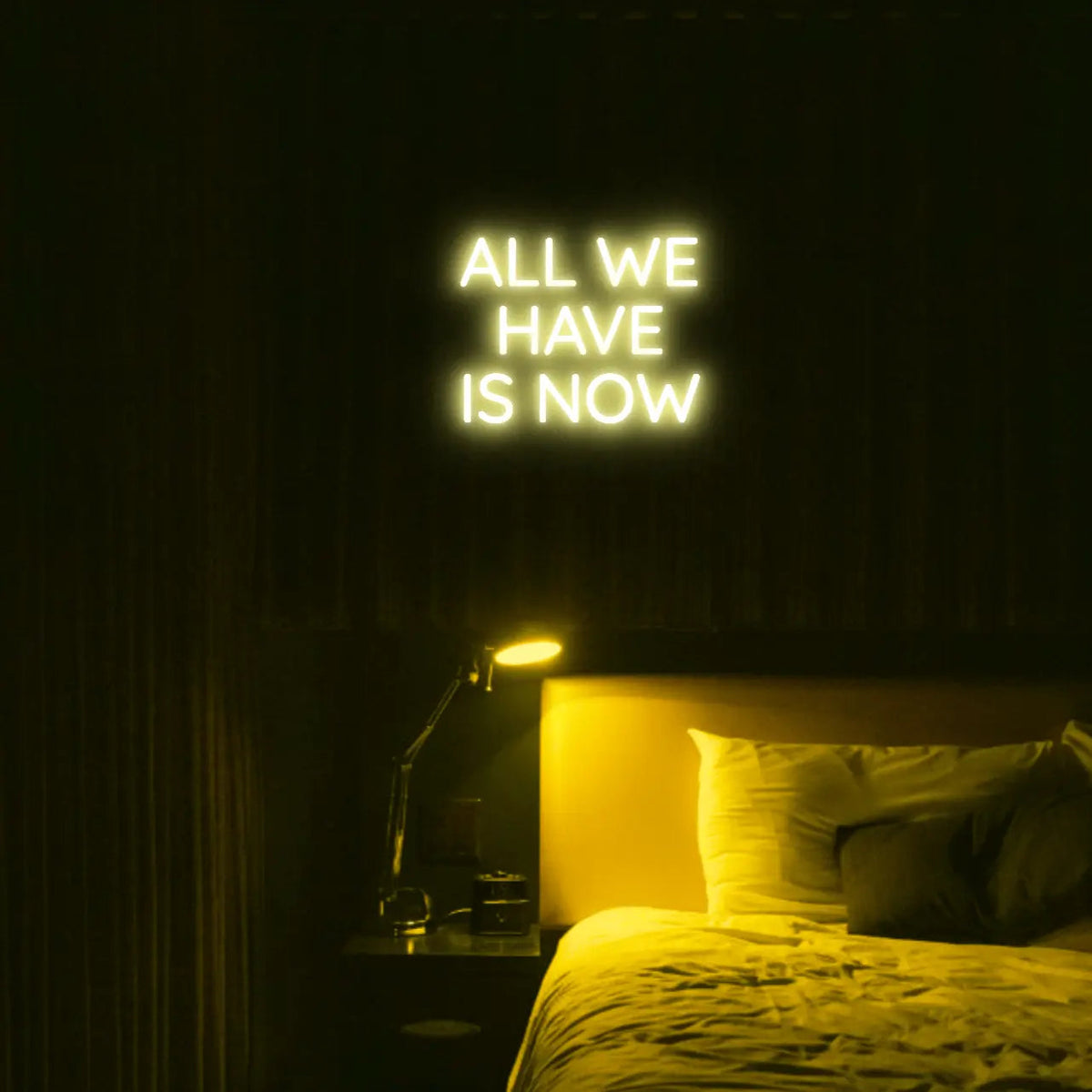 All We Have Is Now LED Neon Light Sign in yellow, featuring three lines of block lettering illuminated above a bed.