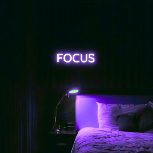 Focus LED Neon Light Sign in purple, featuring block lettering illuminated above a bed.
