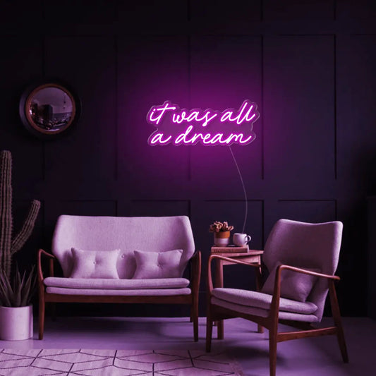 It Was All A Dream LED Neon Sign in pink, featuring script lettering above a small sofa on a dark panelled wall.
