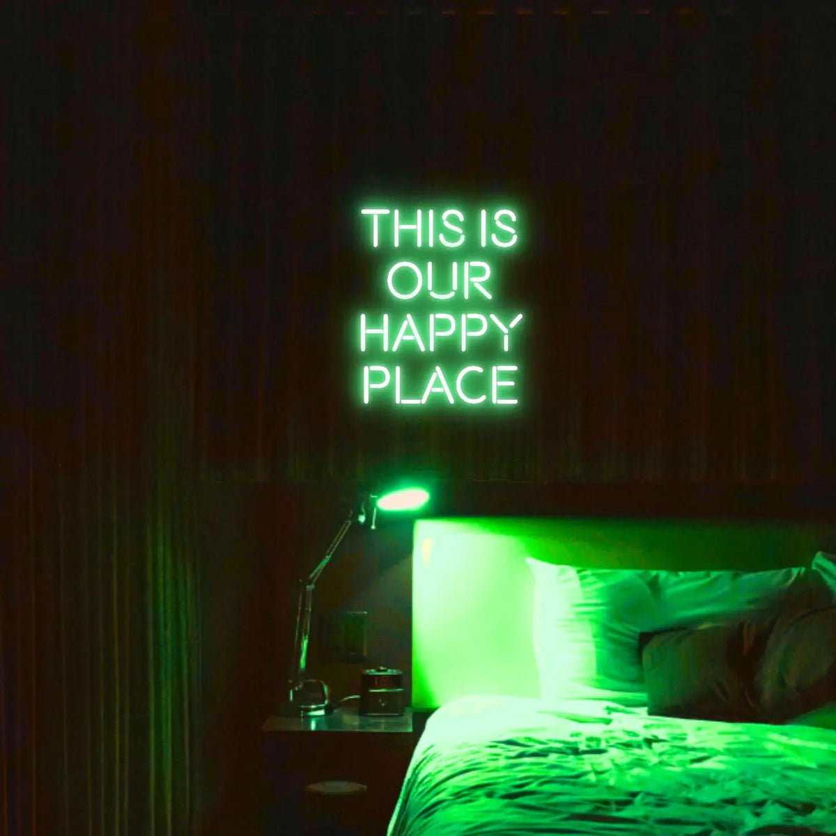 This is our happy place LED Neon Light Sign in green, featuring stacked block lettering illuminated above a bed.