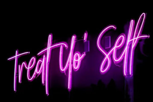 Treat Yo'self LED Neon Light Sign in pink, featuring script lettering viewed at an angle against a dark wall.