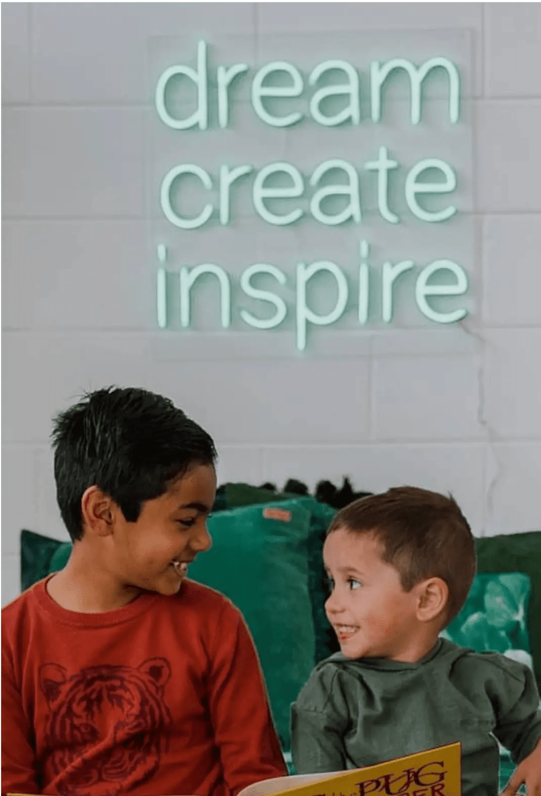 Dream Create Inspire LED Neon Light Sign in mint green, featuring three lines of lettering on a white wall above two children.