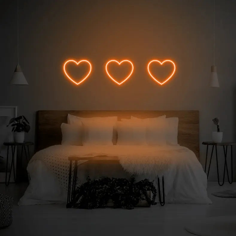 3 Hearts LED Neon Light Sign in orange, featuring three heart outlines illuminated above a bed.