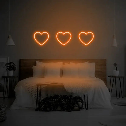3 Hearts LED Neon Light Sign in orange, featuring three heart outlines illuminated above a bed.