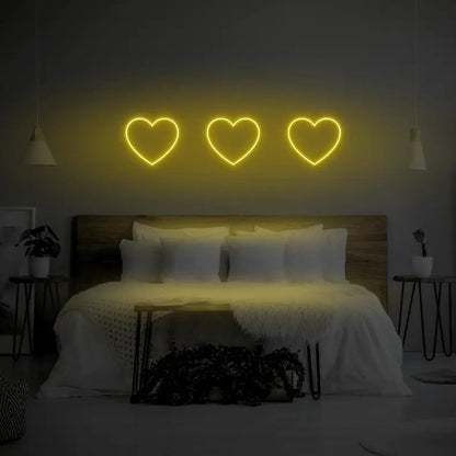 3 Hearts LED Neon Light Sign in yellow, featuring three heart outlines illuminated above a bed.