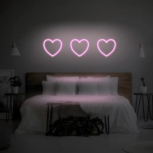 3 Hearts LED Neon Light Sign in pale pink, featuring three heart outlines illuminated above a bed.