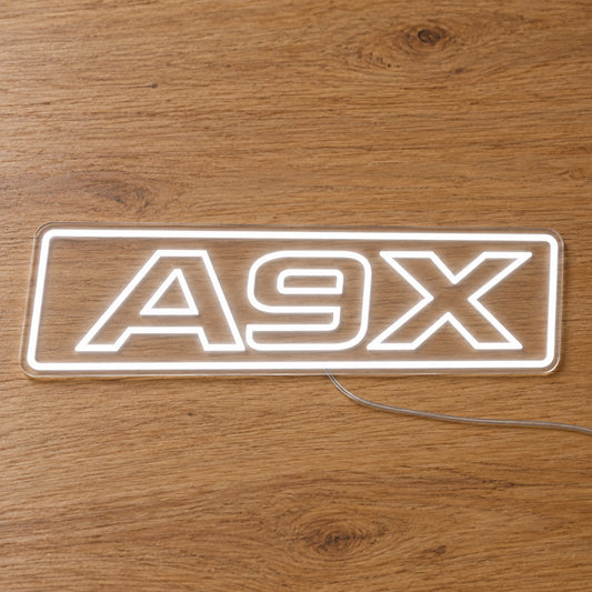 A9X Torana LED Neon Sign in white, featuring A9X lettering inside a rectangular border on a wooden surface.
