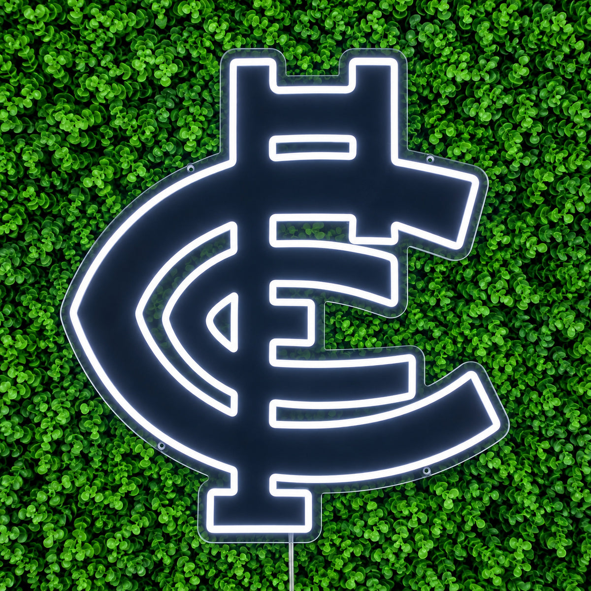 Carlton Blues Neon Sign in white, featuring Carlton monogram against green foliage.