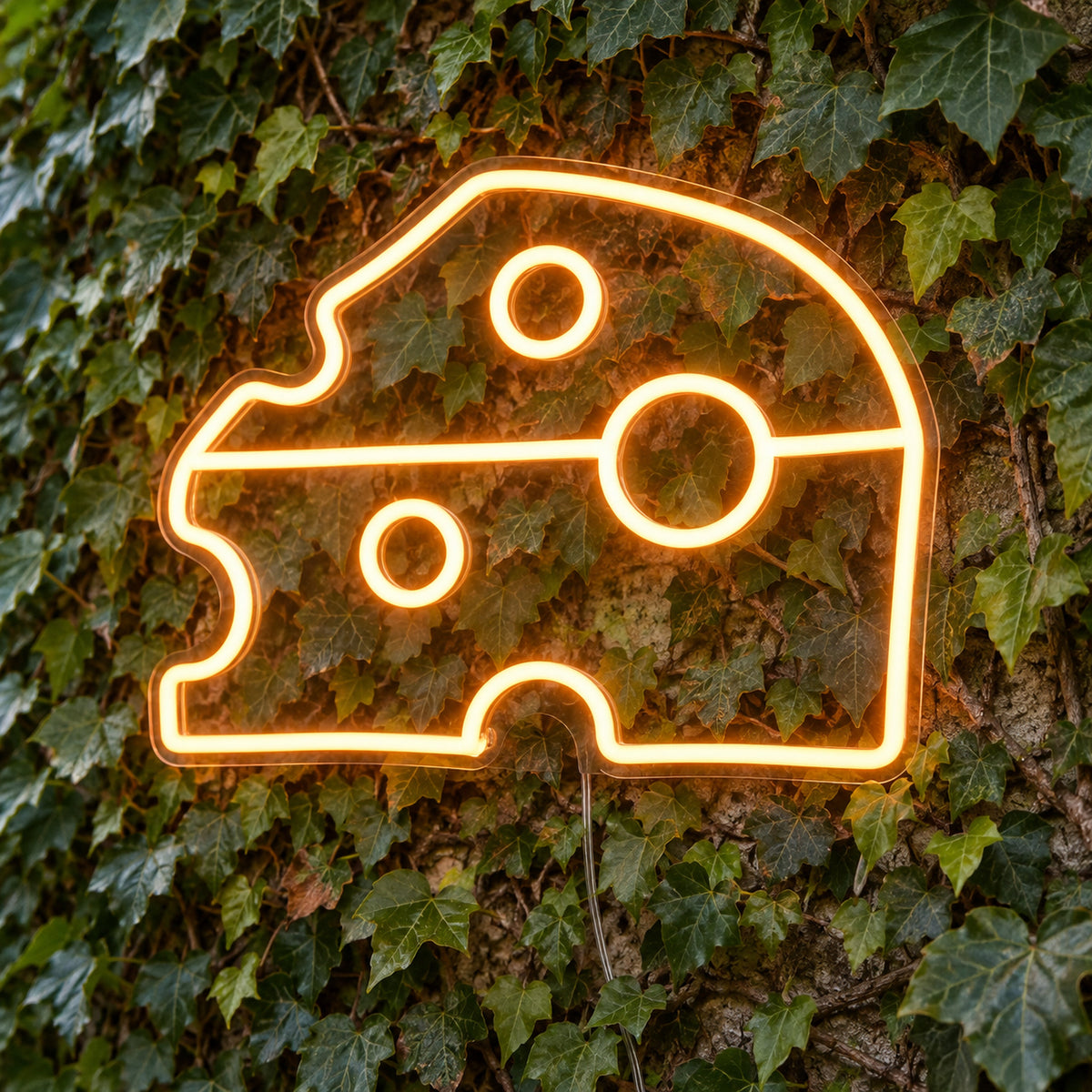 Cheese Block LED Neon Light Sign in yellow, featuring cheese-wedge outline against a foliage wall.