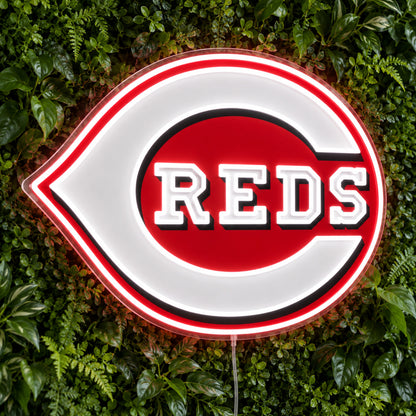 Cincinnati Reds LED Neon Sign, featuring illuminated team logo on a green foliage wall.
