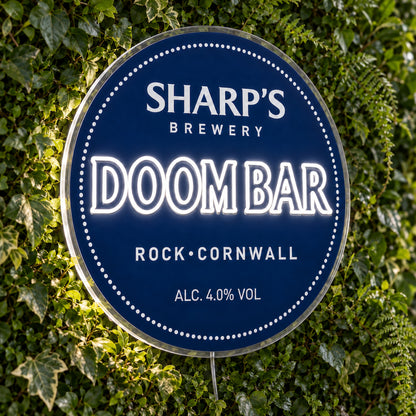 Doom Bar LED Neon Sign, featuring beer-brand logo displayed on a green foliage wall.