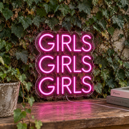 Girls LED Neon Sign in pink, featuring three stacked words against a foliage wall.