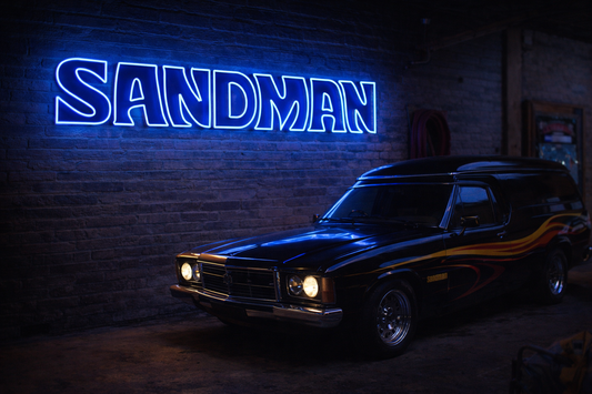 Vintage car in a dark setting with a neon sign reading 'Sandman' on a brick wall.