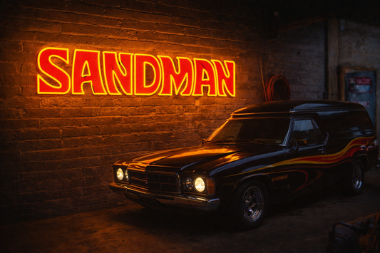 Vintage car parked in a dimly lit garage with a neon 'Sandman' sign on the wall.