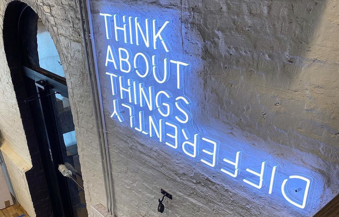 Ice Blue Neon sign saying "think about things differently" on a white wall in Australia Office