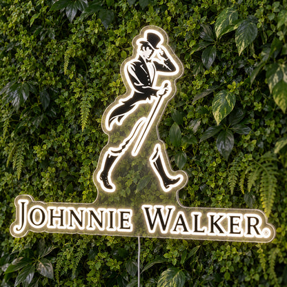 Johnnie Walker LED Neon Sign, featuring illuminated brand logo on a green foliage wall.