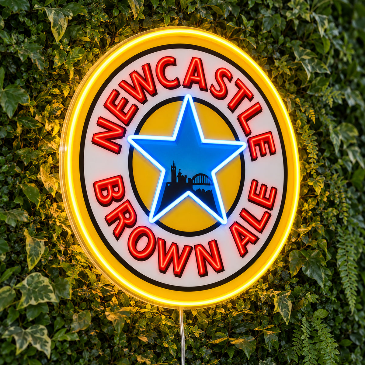 Newcastle Brown Ale LED Neon Sign, featuring beer-brand logo displayed on a green foliage wall.