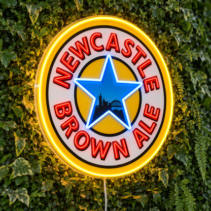 Newcastle Brown Ale LED Neon Sign, featuring beer-brand logo displayed on a green foliage wall.