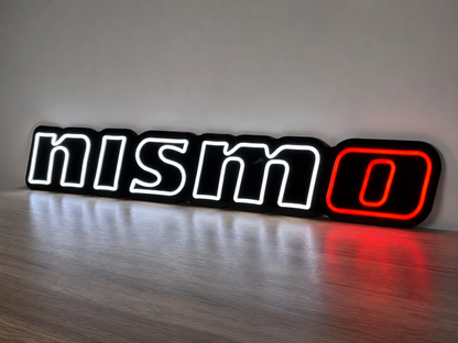 Nissan Nismo LED Neon Sign in white and red, featuring Nismo lettering standing against a grey wall.