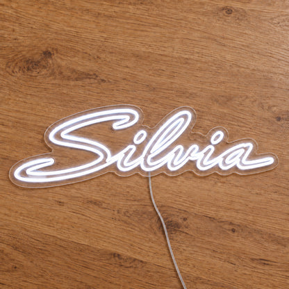 Nissan Silvia LED Neon Sign in white, featuring Silvia script lettering on a wooden surface, wider view.