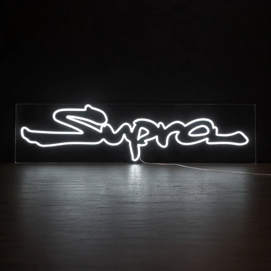 Toyota Supra Logo Neon Sign in white, featuring Supra script logo against a dark wall.
