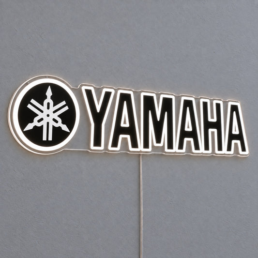 Yamaha (Black) LED Neon Sign in white, featuring Yamaha lettering beside a tuning-fork emblem on a grey wall.