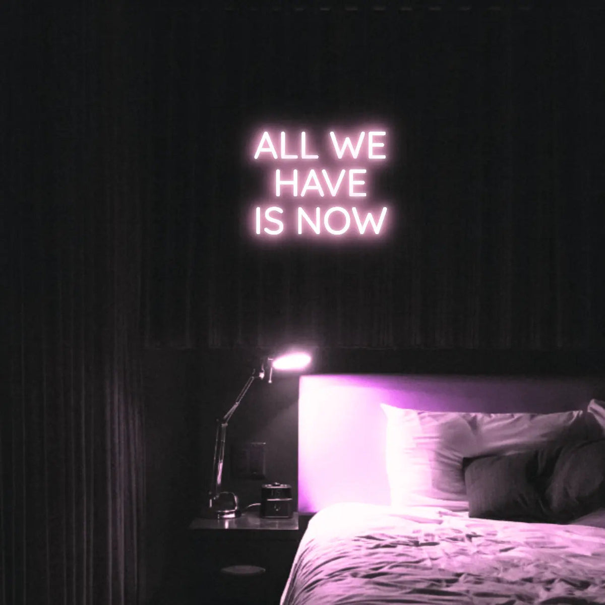 All We Have Is Now LED Neon Light Sign in pale pink, featuring three lines of block lettering illuminated above a bed.