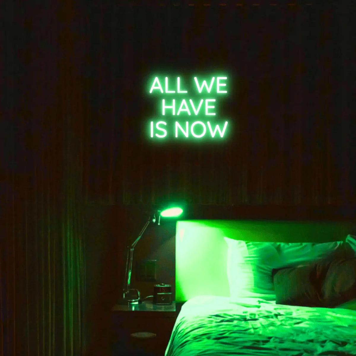 All We Have Is Now LED Neon Light Sign in green, featuring three lines of block lettering illuminated above a bed.
