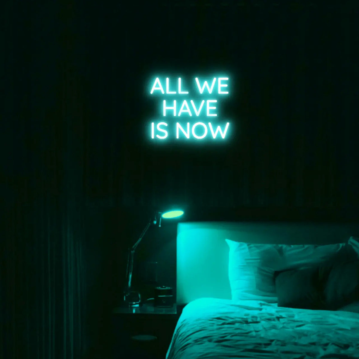 All We Have Is Now LED Neon Light Sign in turquoise, featuring three lines of block lettering illuminated above a bed.