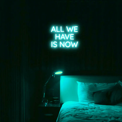 All We Have Is Now LED Neon Light Sign in turquoise, featuring three lines of block lettering illuminated above a bed.