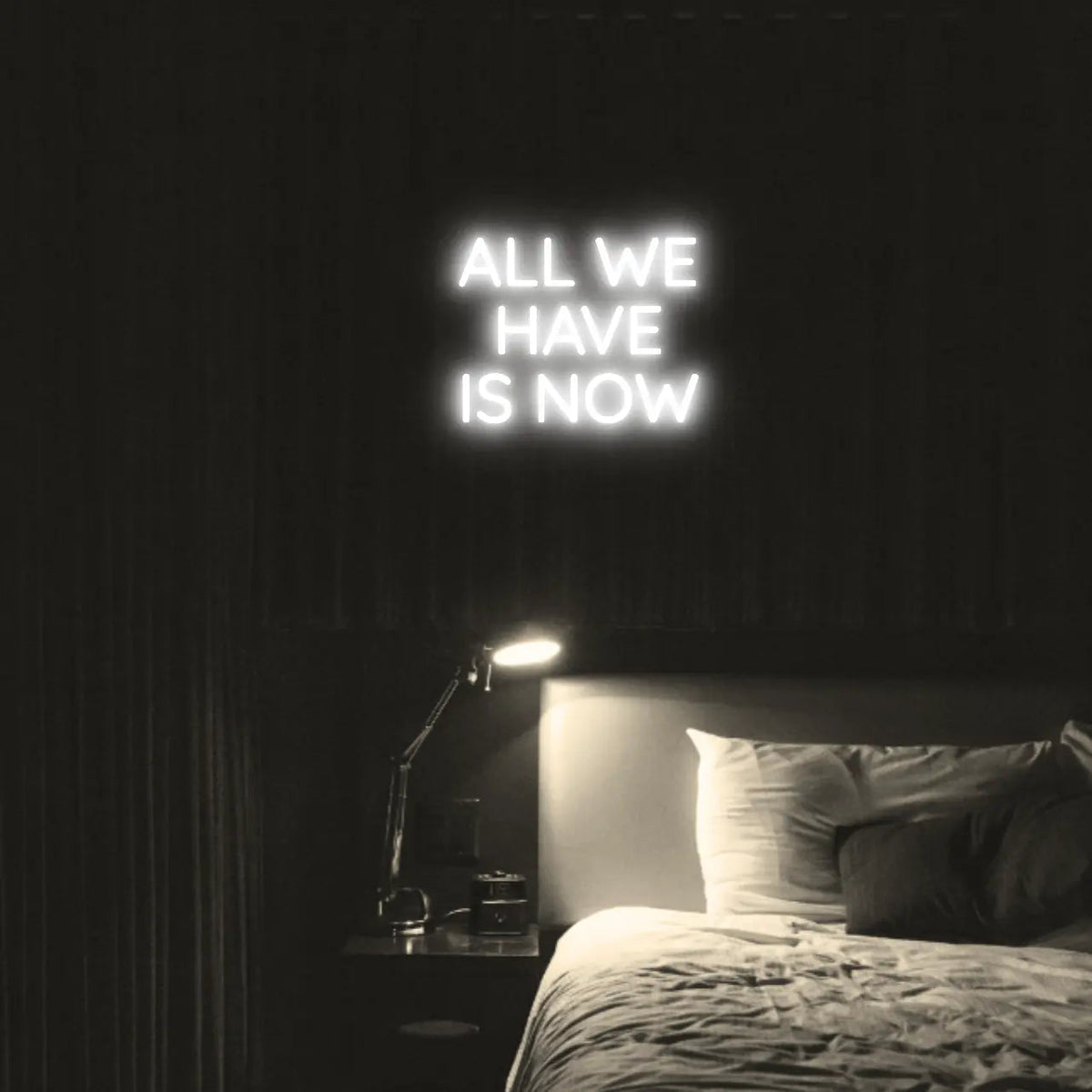 All We Have Is Now LED Neon Light Sign in white, featuring three lines of block lettering illuminated above a bed.