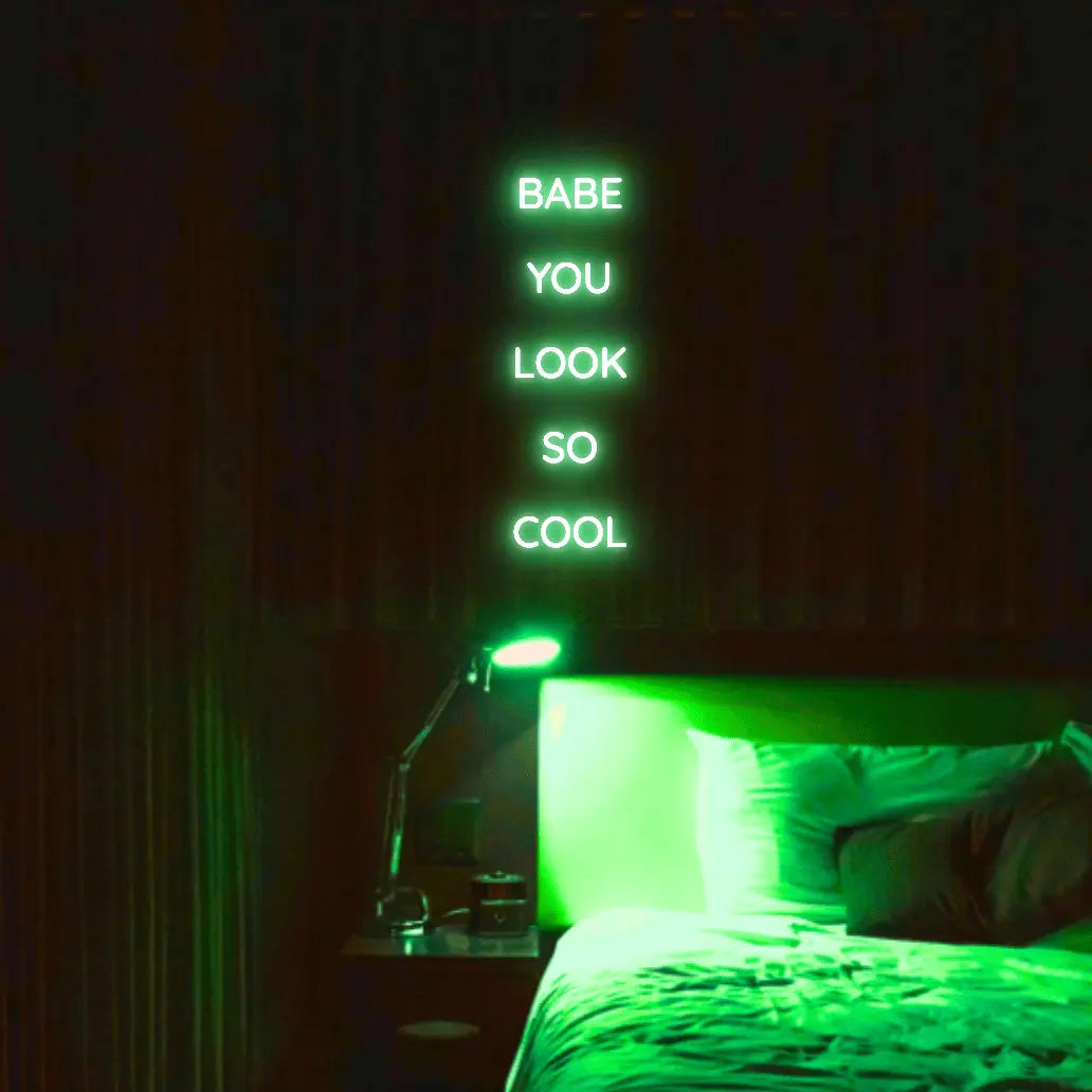 Babe You Look So Cool 2 LED Neon Light Sign in green, featuring five stacked words illuminated above a bed.