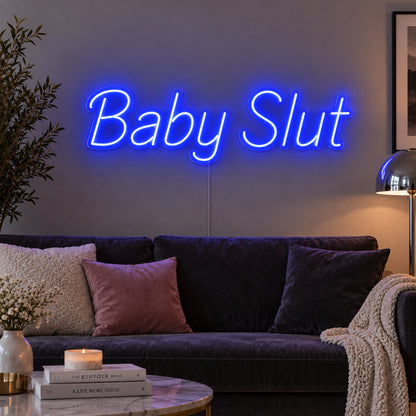 Baby Slut Neon Sign glowing blue above a grey sofa with pink cushions.