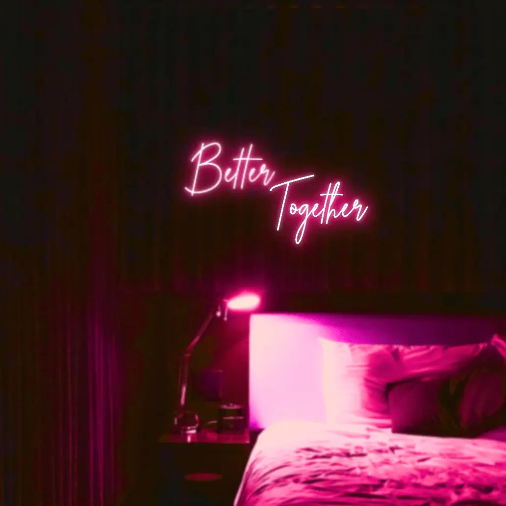Better Together LED Neon Light Sign in pink, featuring two lines of script lettering illuminated above a bed.