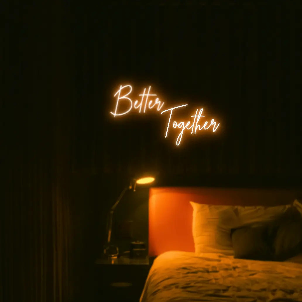 Better Together LED Neon Light Sign in orange, featuring two lines of script lettering illuminated above a bed.