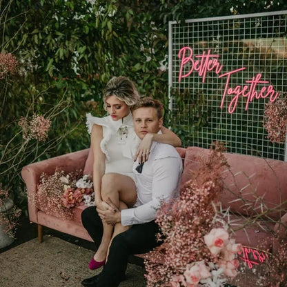 Better Together LED Neon Light Sign in pink, featuring script lettering on a wire-grid wedding backdrop behind a seated couple.