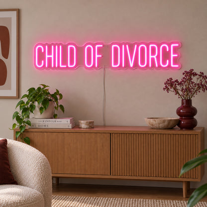 Rose Red version of the Child Of Divorce Neon Sign, shown above a wooden sideboard with plants.