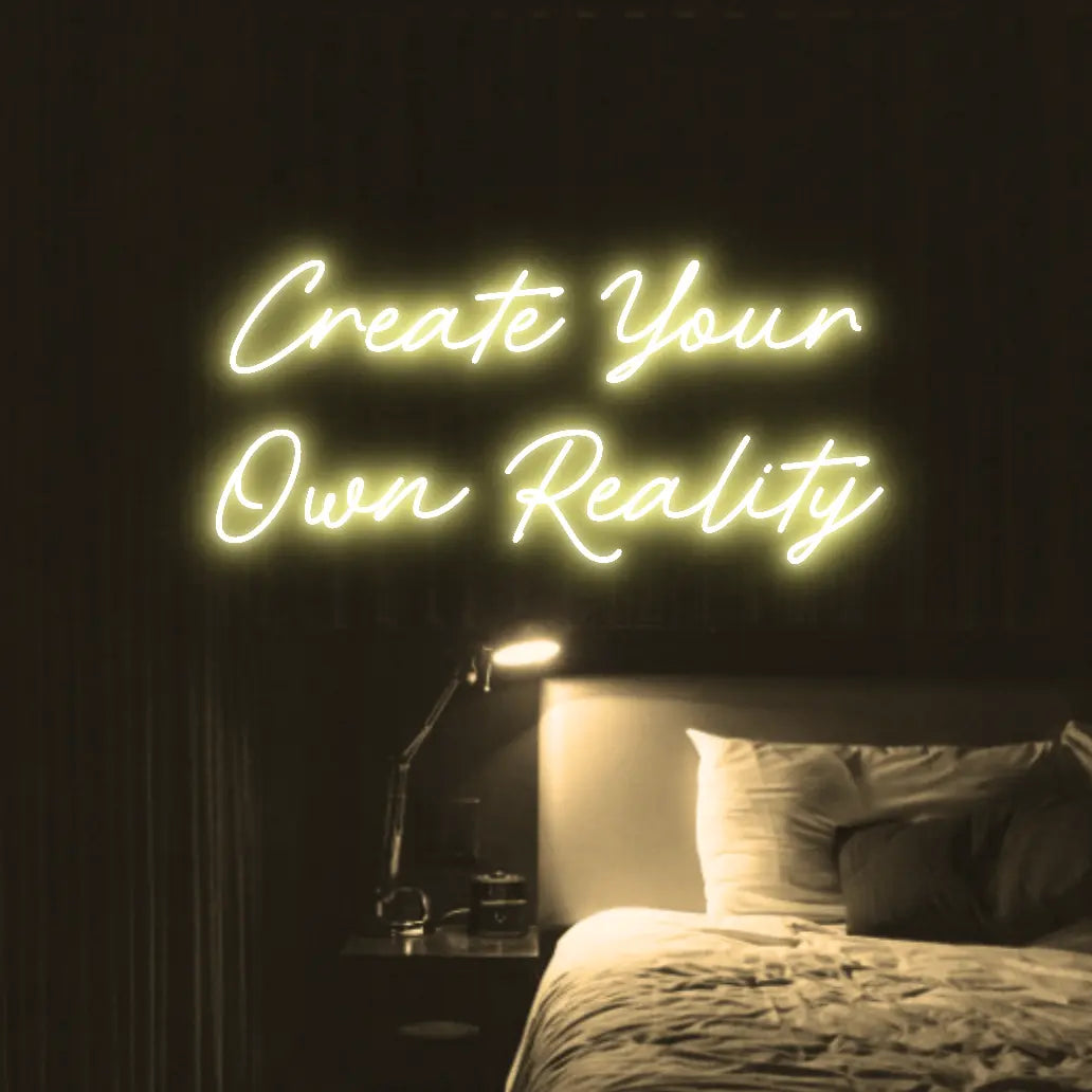 Create Your Own Reality LED Neon Light Sign in warm white, featuring two lines of script lettering illuminated above a bed.