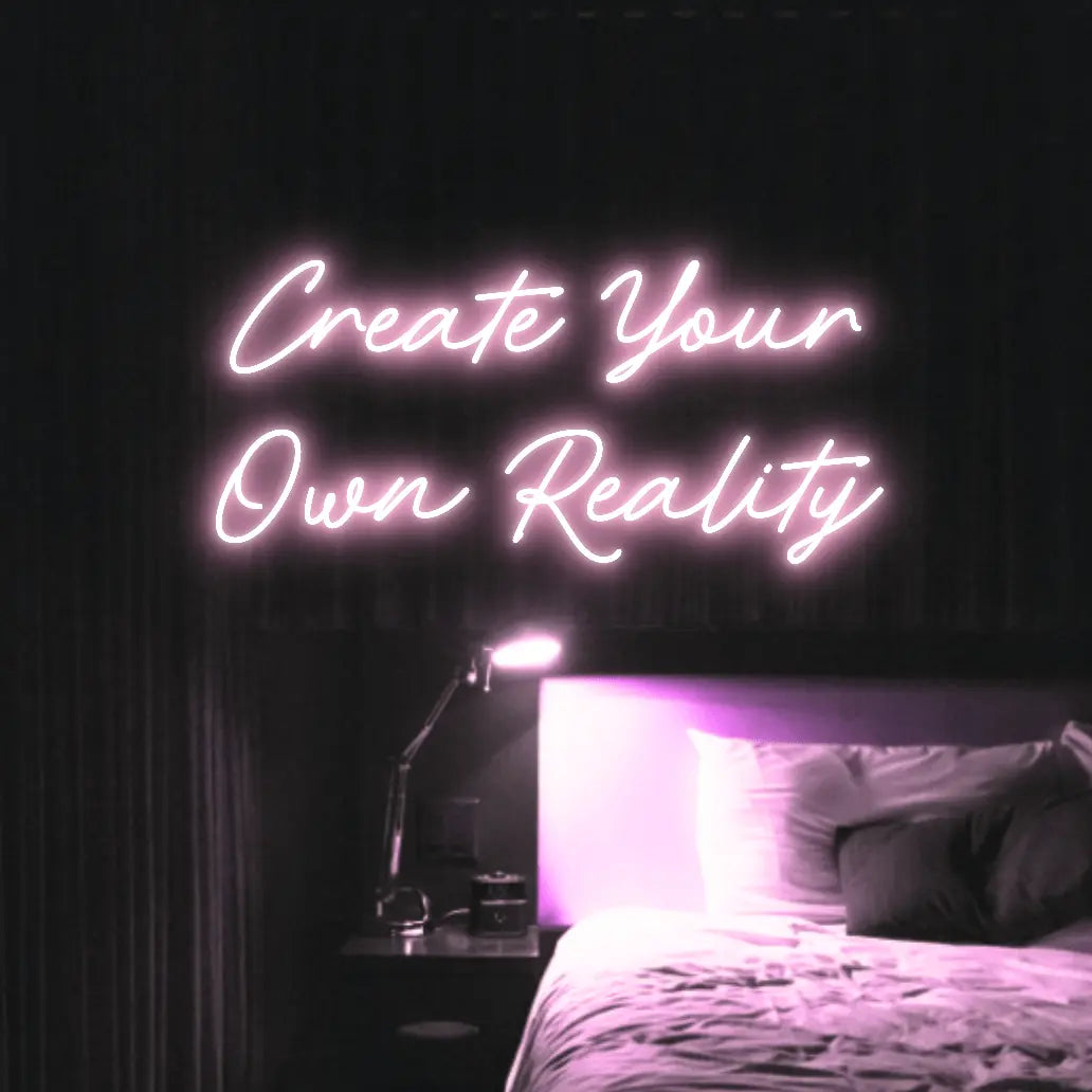Create Your Own Reality LED Neon Light Sign in pale pink, featuring two lines of script lettering illuminated above a bed.