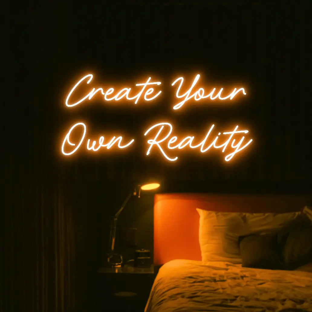 Create Your Own Reality LED Neon Light Sign in orange, featuring two lines of script lettering illuminated above a bed.