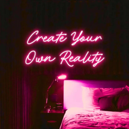 Create Your Own Reality LED Neon Light Sign in pink, featuring two lines of script lettering illuminated above a bed.