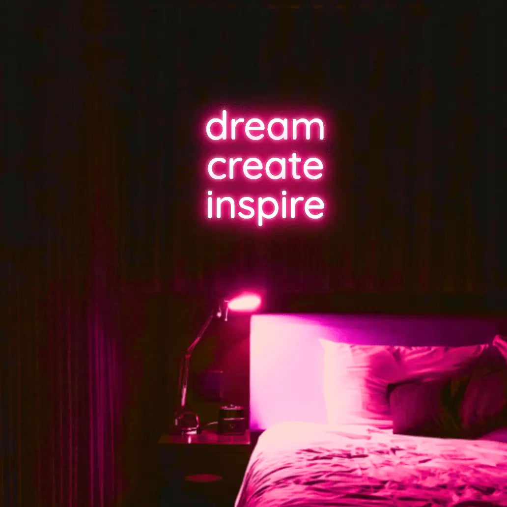 Dream Create Inspire LED Neon Light Sign in pink, featuring three lines of lettering illuminated above a bed.