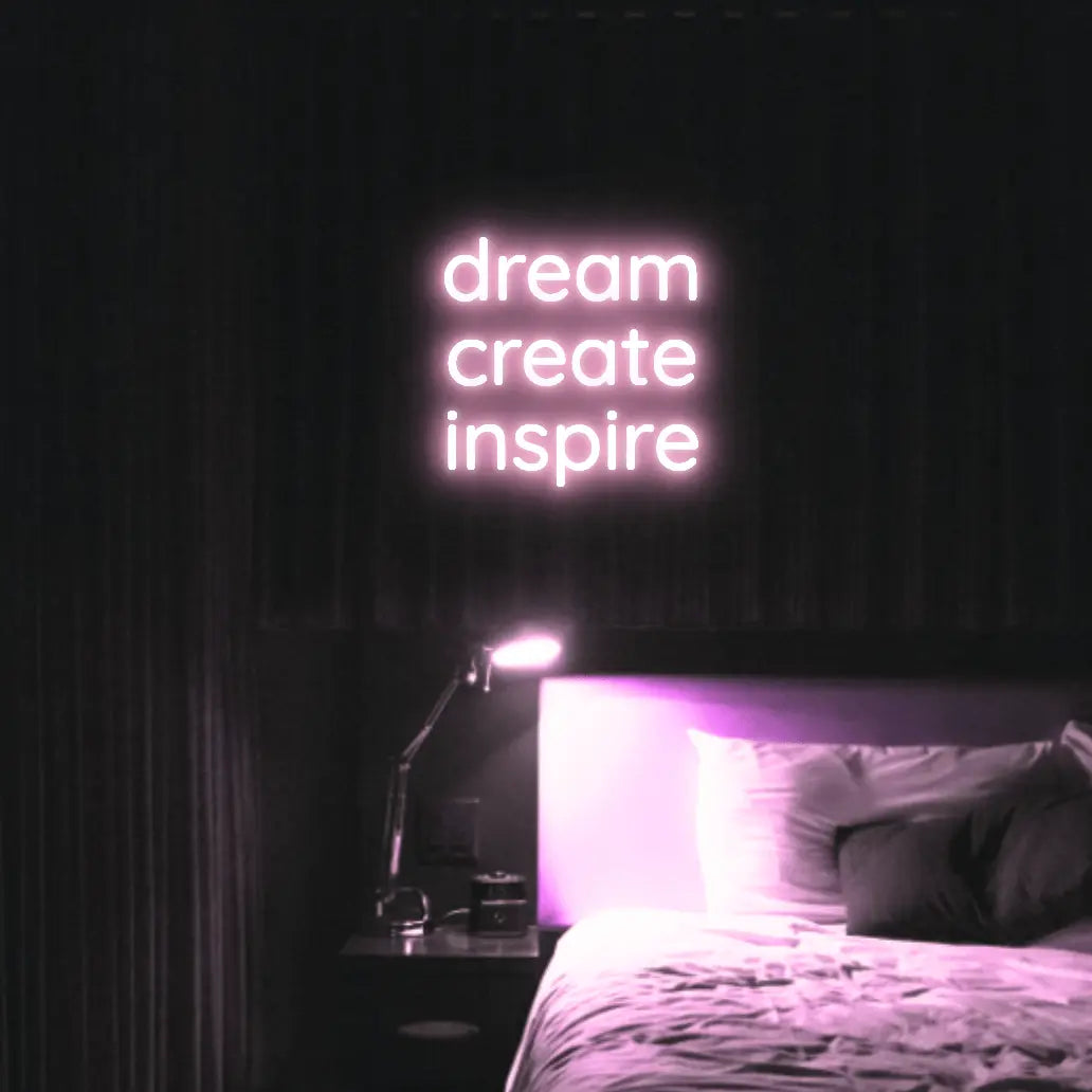 Dream Create Inspire LED Neon Light Sign in pale pink, featuring three lines of lettering illuminated above a bed.
