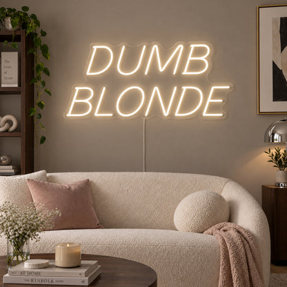 Warm White version of the Dumb Blonde Neon Sign, shown in slanted lettering above a cream sofa.