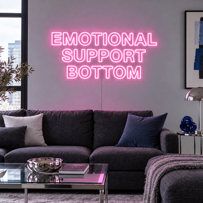Emotional Support Bottom Neon Sign glowing pink above a charcoal sofa.