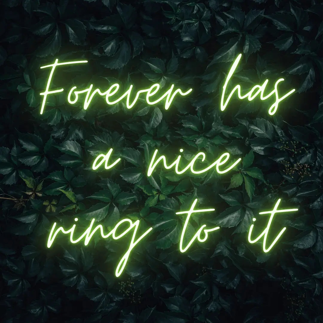 Forever Has a Nice Ring to It LED Neon Light Sign in lime green, featuring three lines of script lettering against a dark foliage backdrop.